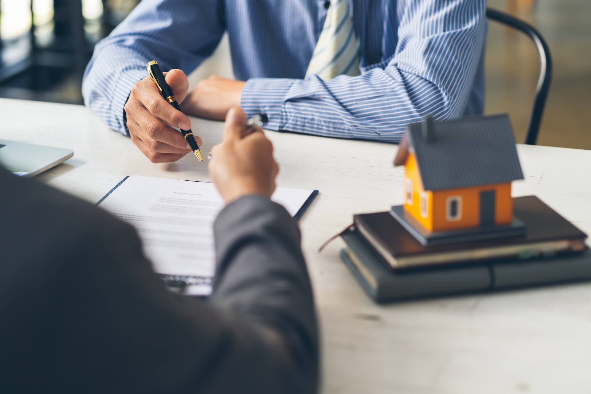 Real estate home are pointing to insurance contract signing and are explaining to customers at the office. house agency concept.